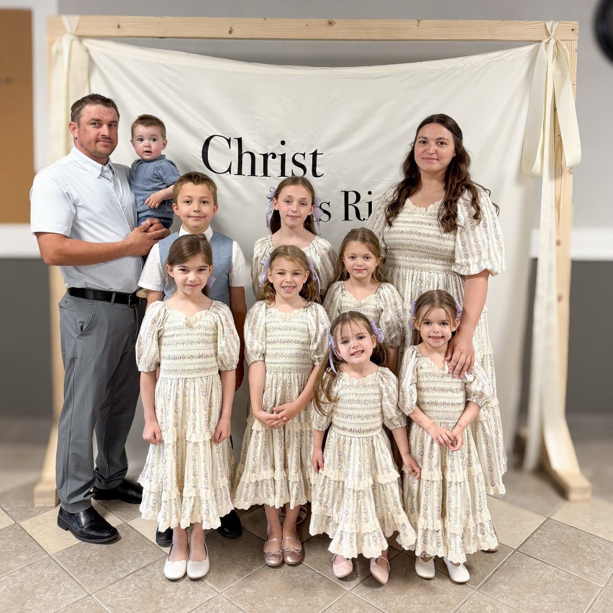 A large family posing together wearing coordinated white floral and neutral colored outfits.