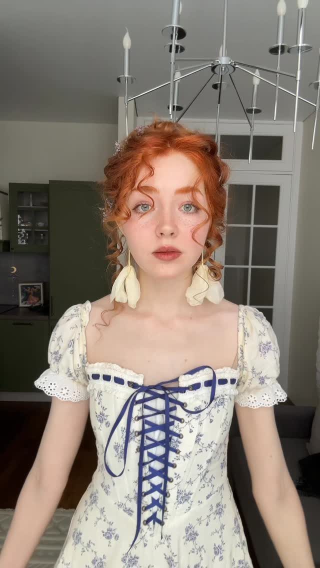 Red-haired woman wearing a white and blue floral puff-sleeve dress with a lace-up bodice.