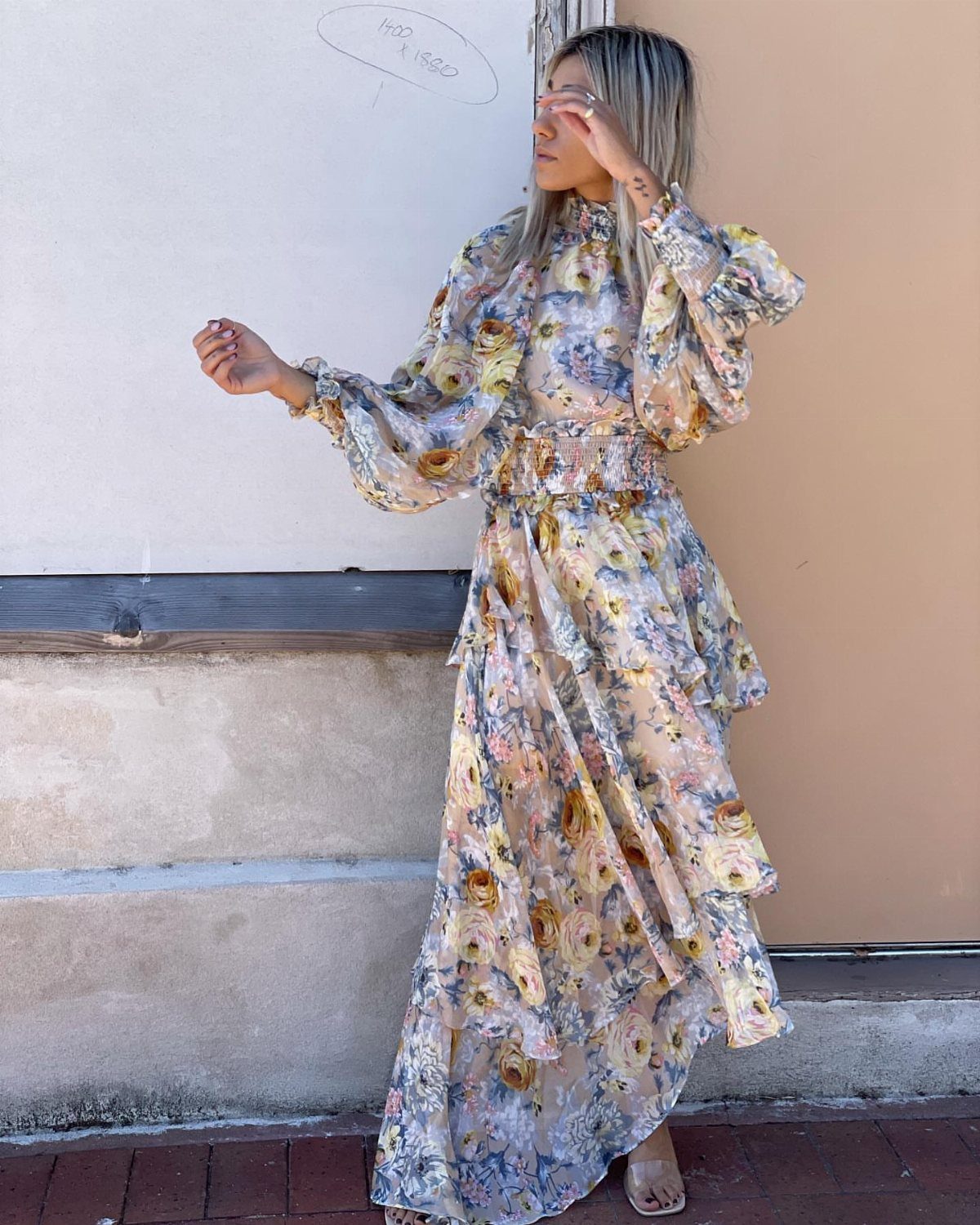 A woman posing in a long, flowing floral print maxi dress with voluminous sleeves.