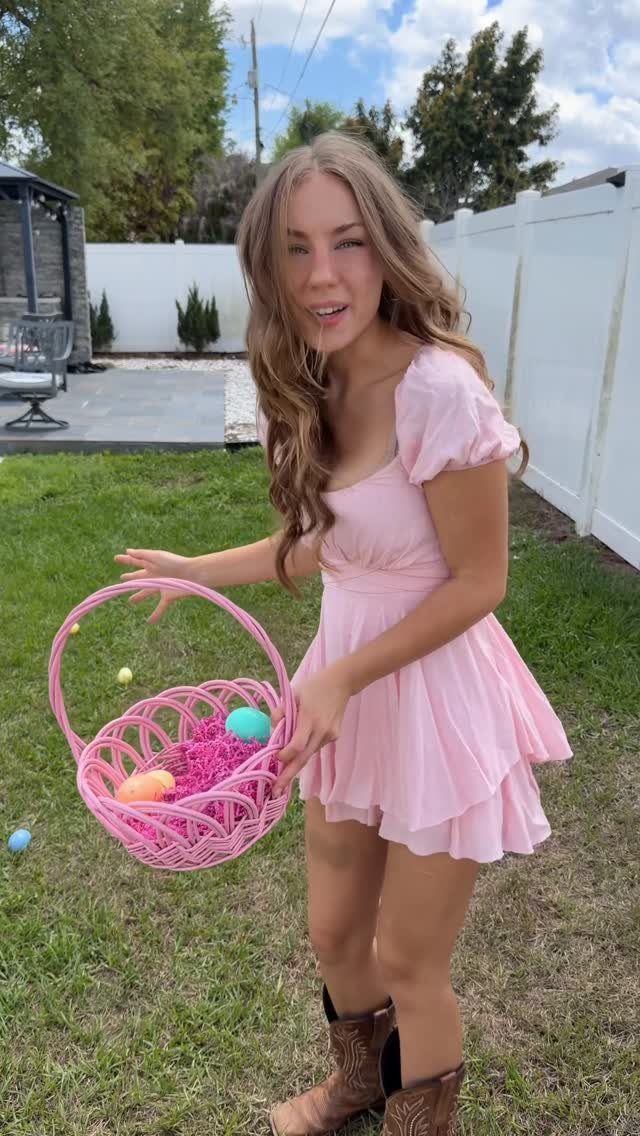 A woman in a pink dress holding a pink Easter basket filled with colorful eggs.