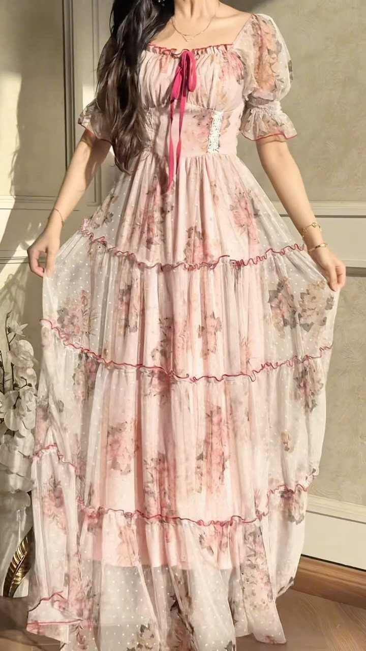 Woman wearing a long, pink floral print dress with puff sleeves and red ribbon details.