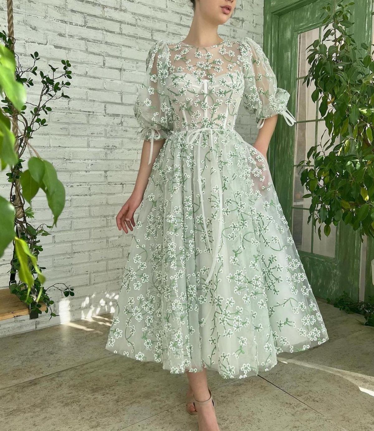 Woman wearing a light green floral embroidered midi dress with puff sleeves standing outdoors.