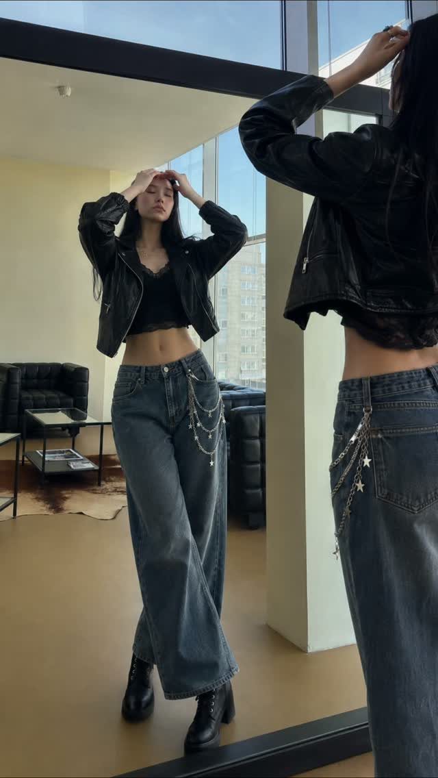 Woman posing in a black leather jacket, black crop top, and wide-leg denim jeans.