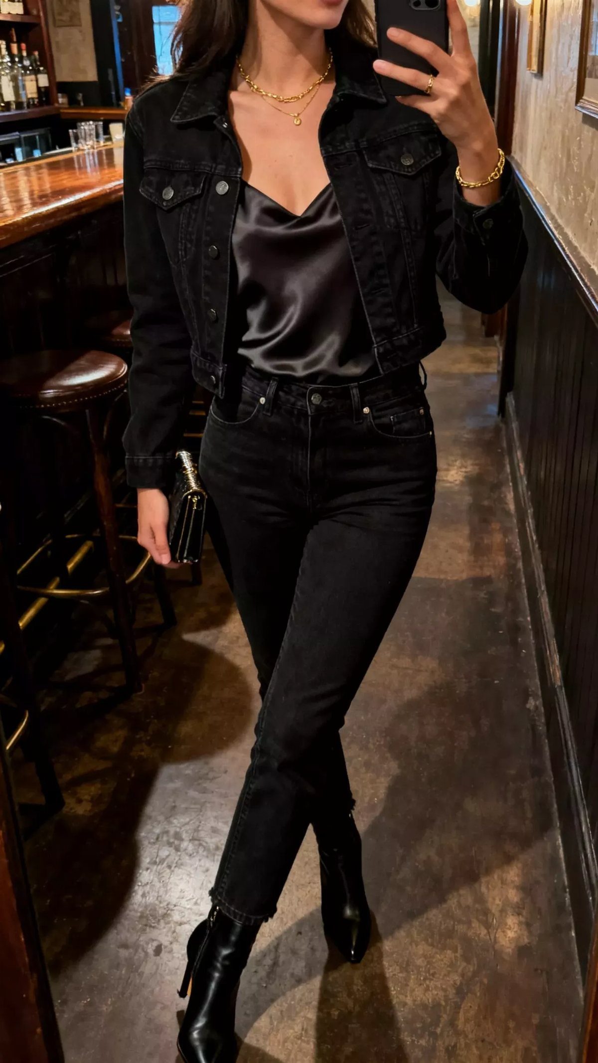 Woman wearing a black satin top, denim jacket, black jeans, and gold jewelry.