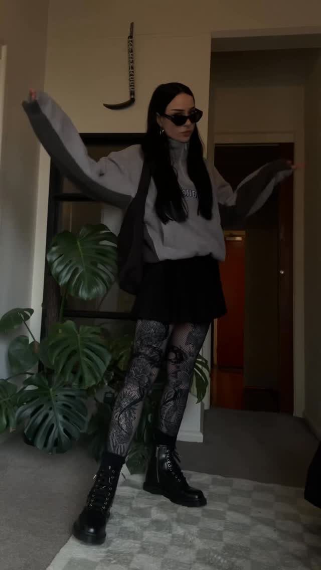 Person wearing a grey sweatshirt, black skirt, patterned tights, and black chunky combat boots.