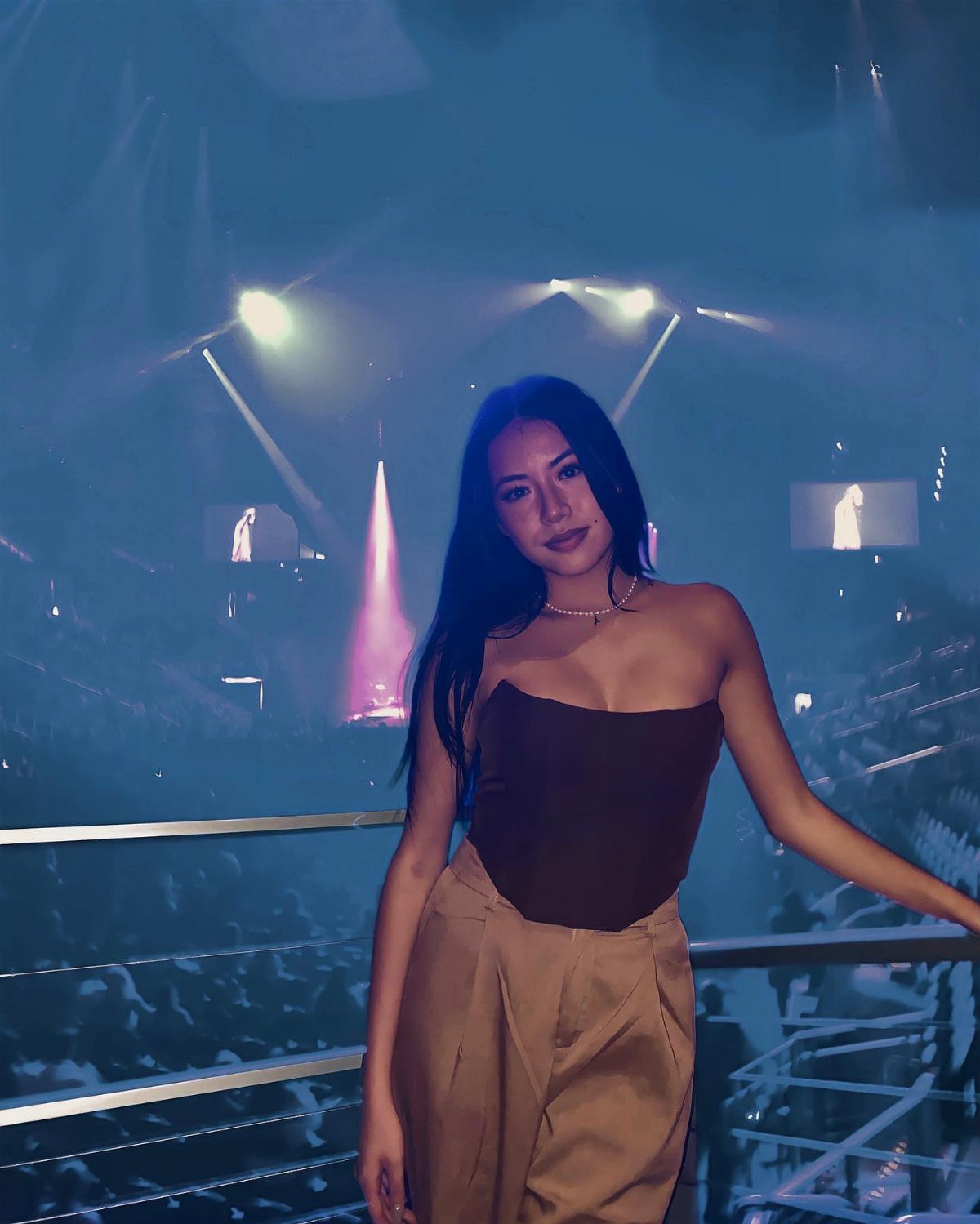 A woman wearing a dark brown strapless corset top and tan pants at a concert.