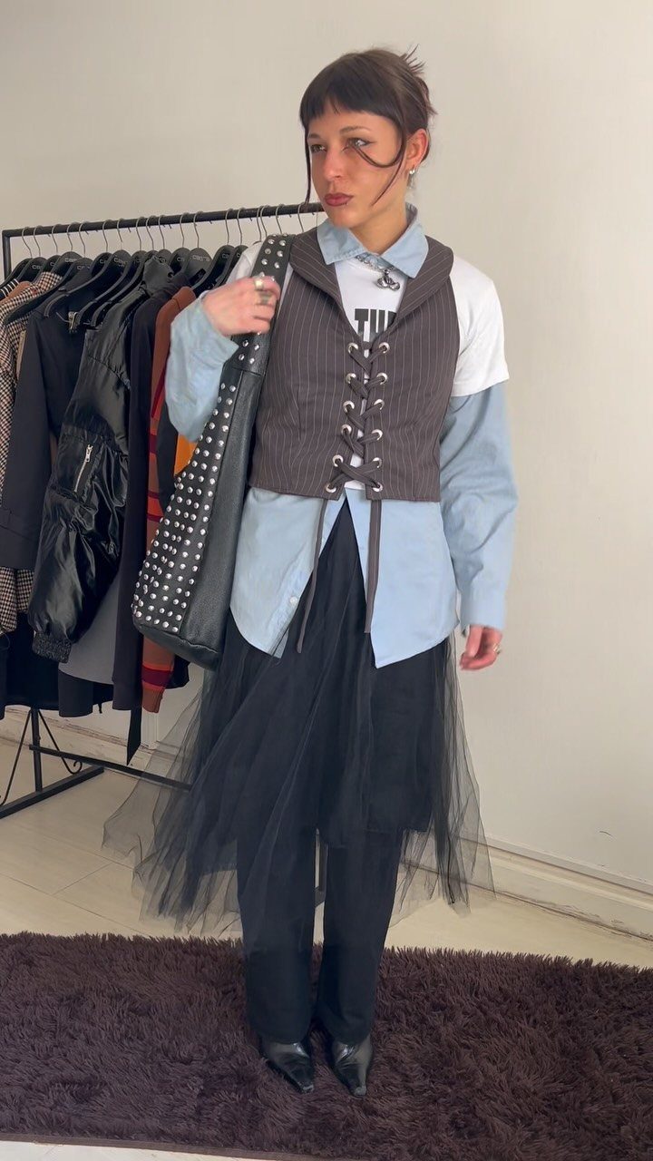 A person posing in a layered outfit with a corset vest, blue shirt, and tulle skirt.