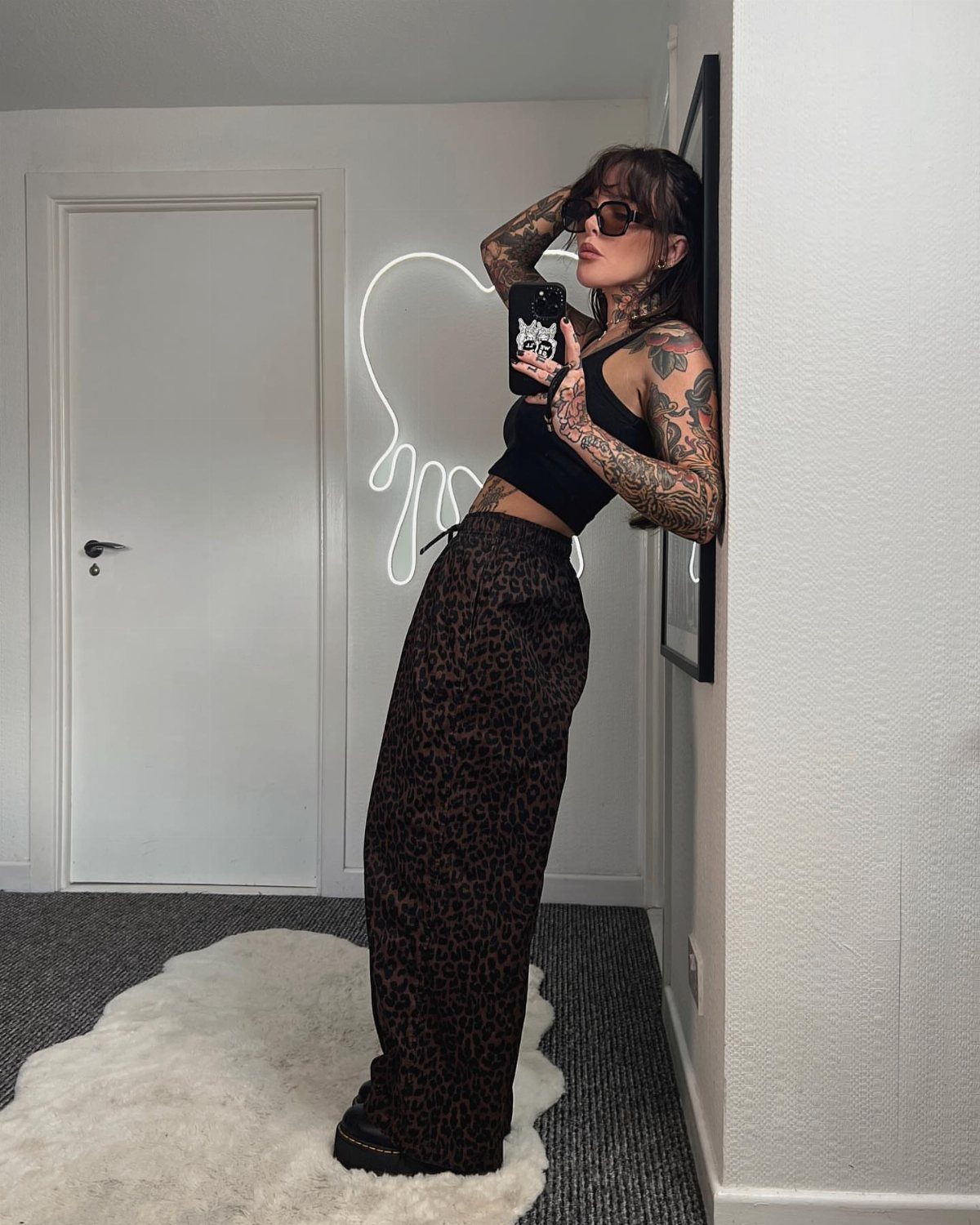 Woman in leopard print high-waisted pants and black crop top posing for a selfie.