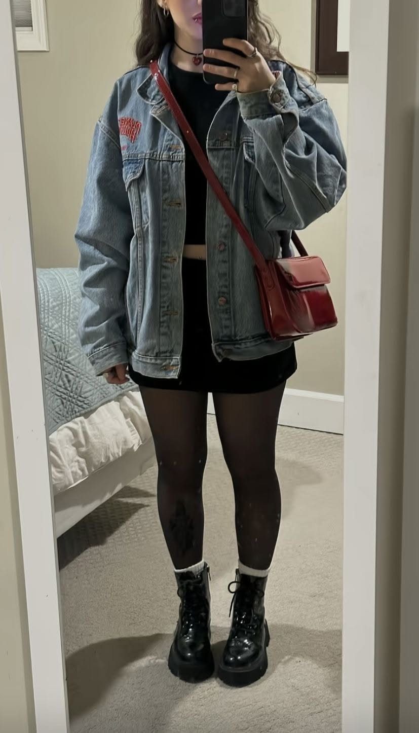 Person wearing an oversized denim jacket, black crop top, mini skirt, and chunky combat boots.