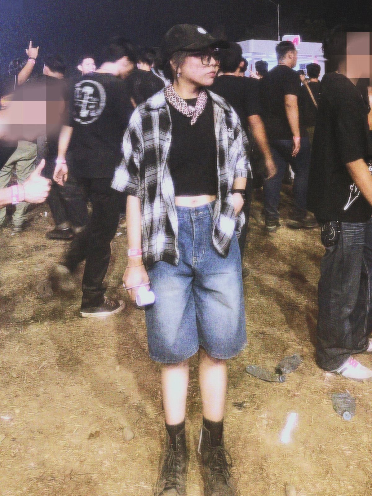 Person wearing a black and white plaid flannel shirt, black crop top, and denim shorts at a night event.