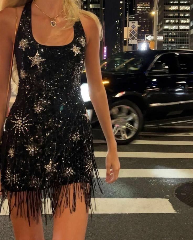 A person wearing a black sequined mini dress with silver stars and fringe on a city street.