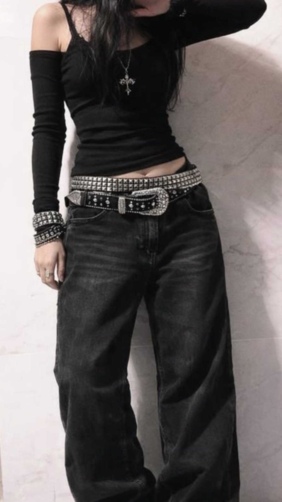 Person wearing black baggy jeans with two wide silver studded belts and a cross necklace.