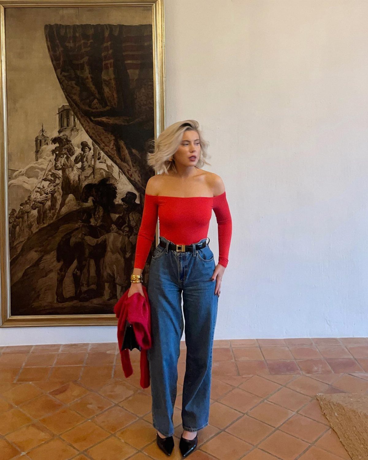 Blonde woman posing in a red off-the-shoulder top and blue wide-leg denim jeans.