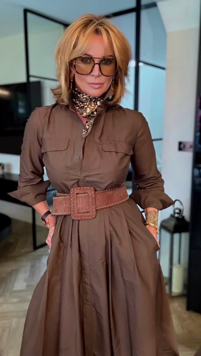Blonde woman wearing a brown long-sleeved dress with a wide belt and patterned scarf.