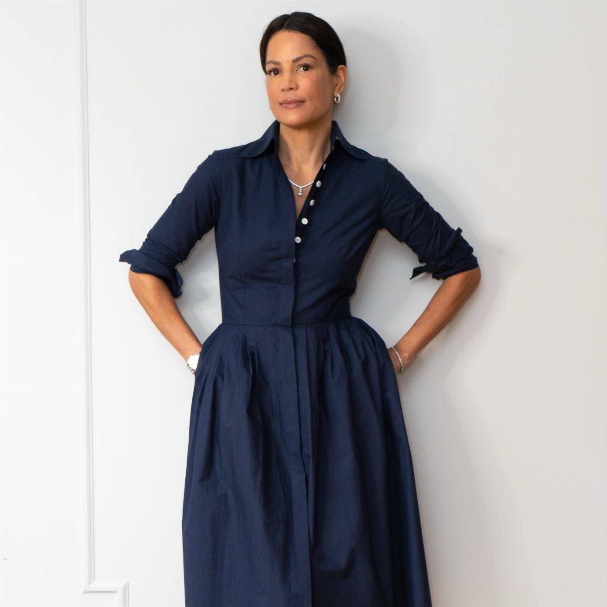 Woman posing in a navy blue cotton poplin shirtdress with a button-down front and cinched waist.