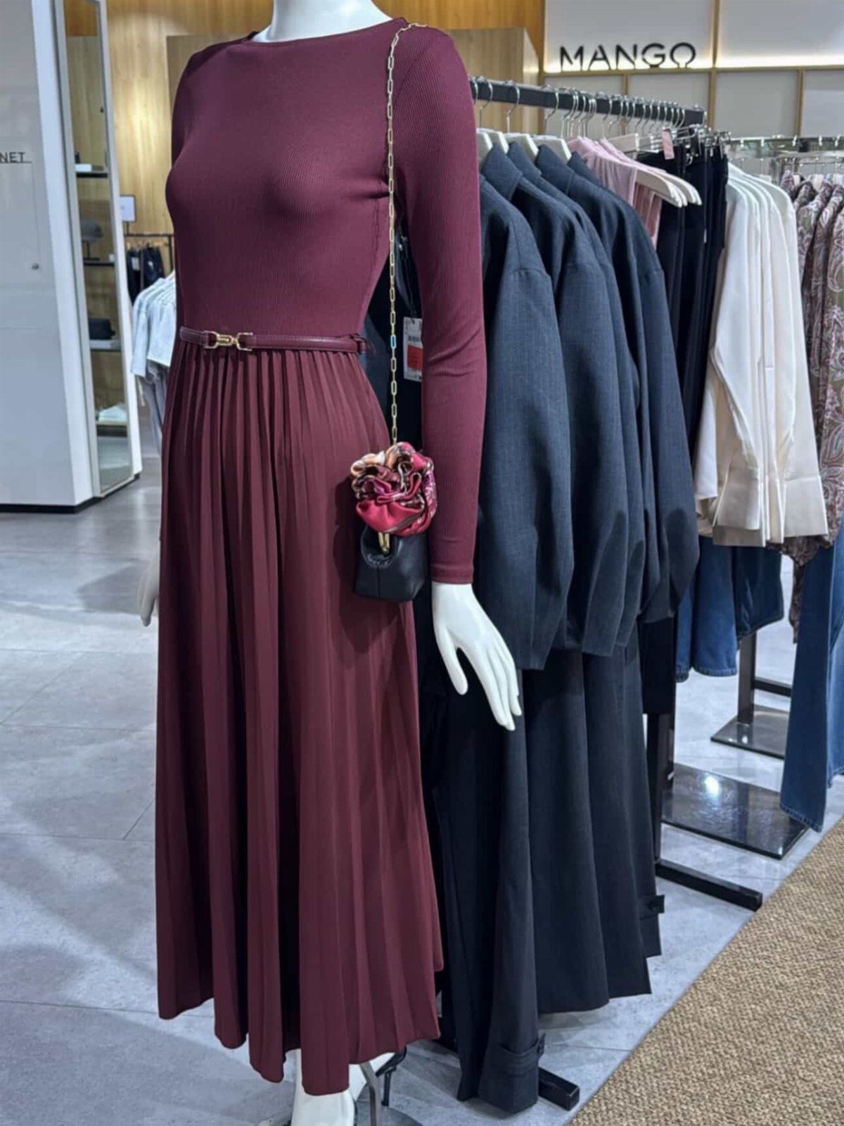 Burgundy long-sleeved pleated midi dress displayed on a mannequin in a clothing store.