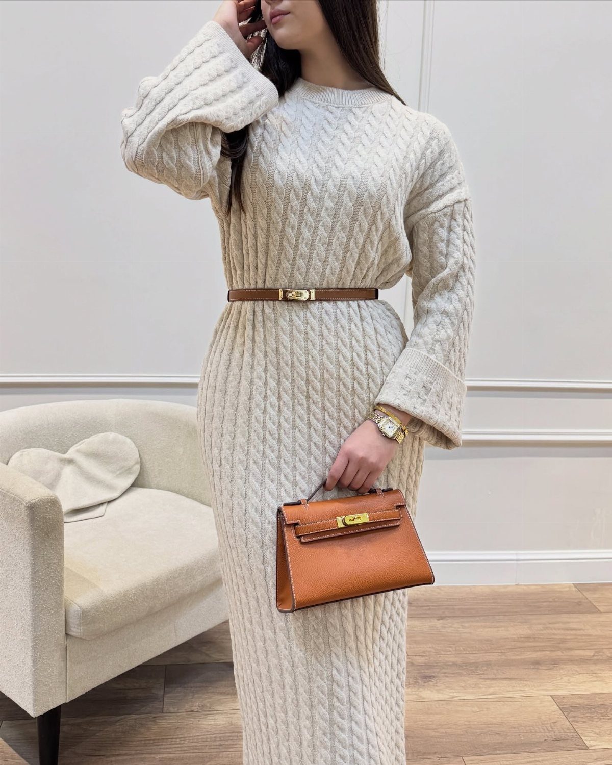 Woman wearing a cream cable-knit sweater maxi dress with a brown belt and handbag.