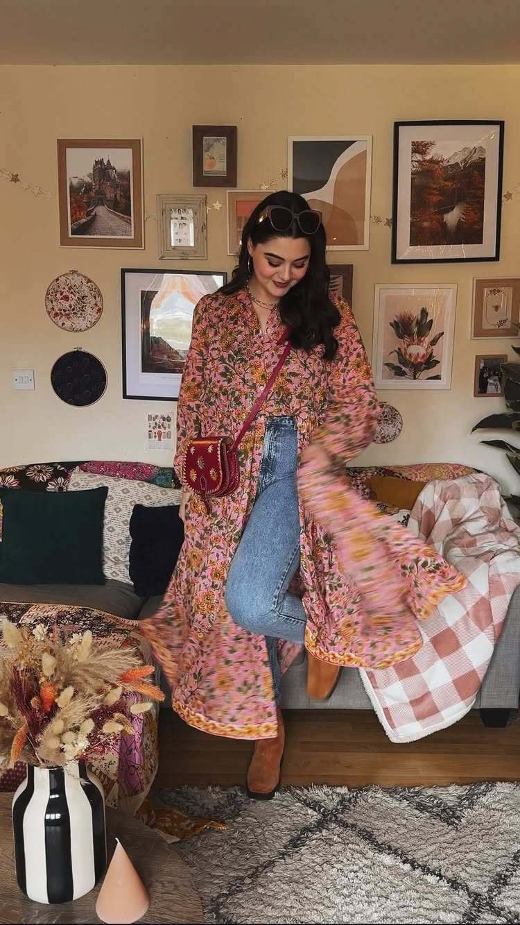Woman wearing a long floral dress layered over blue jeans and brown boots.