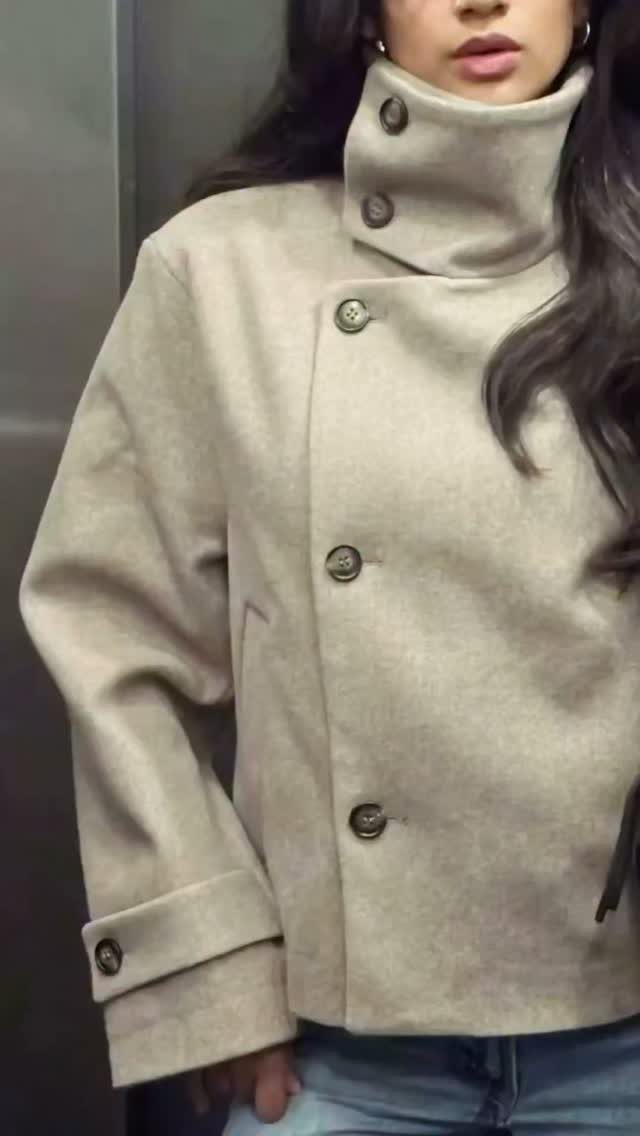 A woman wearing a beige high-collared wool coat and blue jeans.
