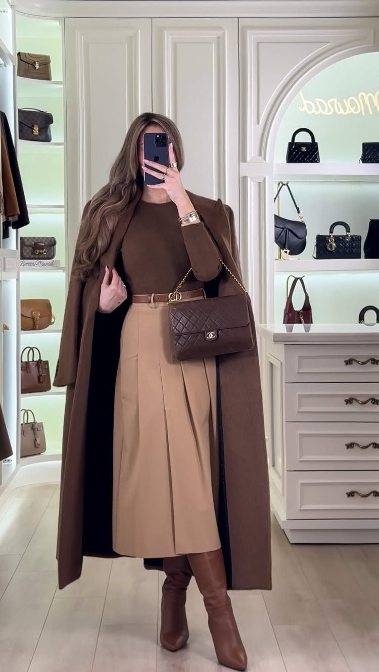 Woman wearing a brown coat, tan skirt, and brown boots standing in a boutique.