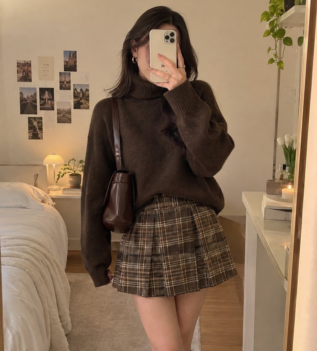 Woman in a brown turtleneck and plaid skirt posing for a mirror selfie.