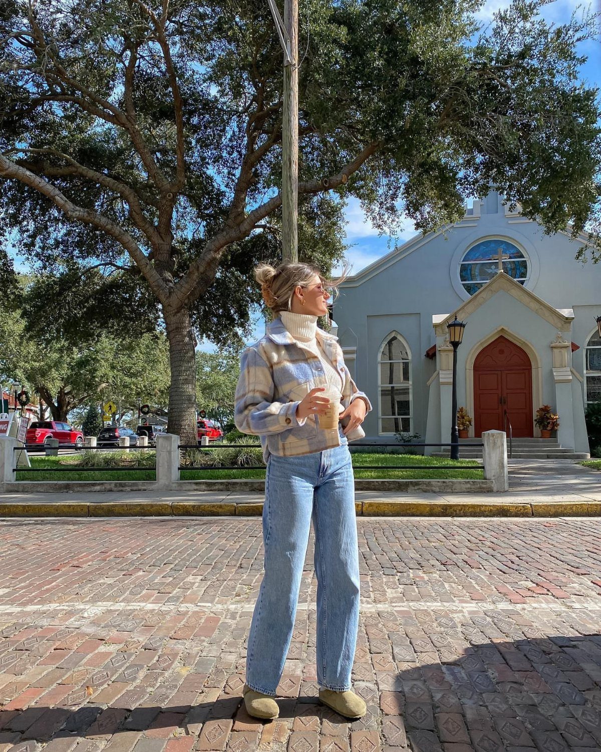 Woman wearing a cream turtleneck and wide-leg blue jeans standing on a brick street.