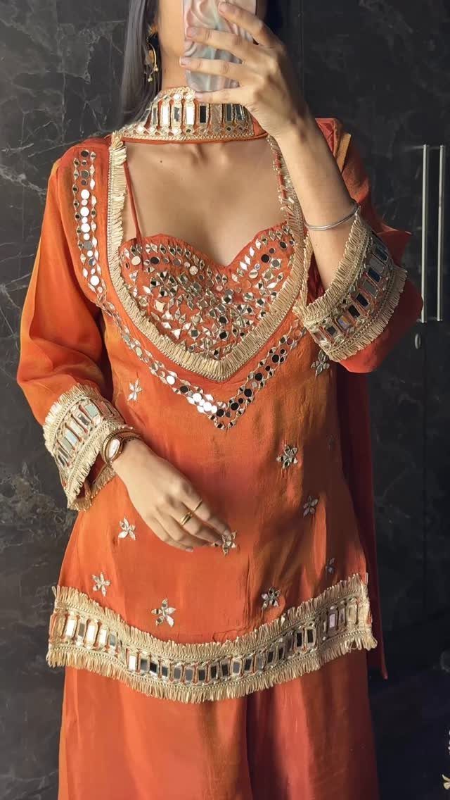 Person in an orange traditional outfit with gold embroidery and mirror work taking a selfie.