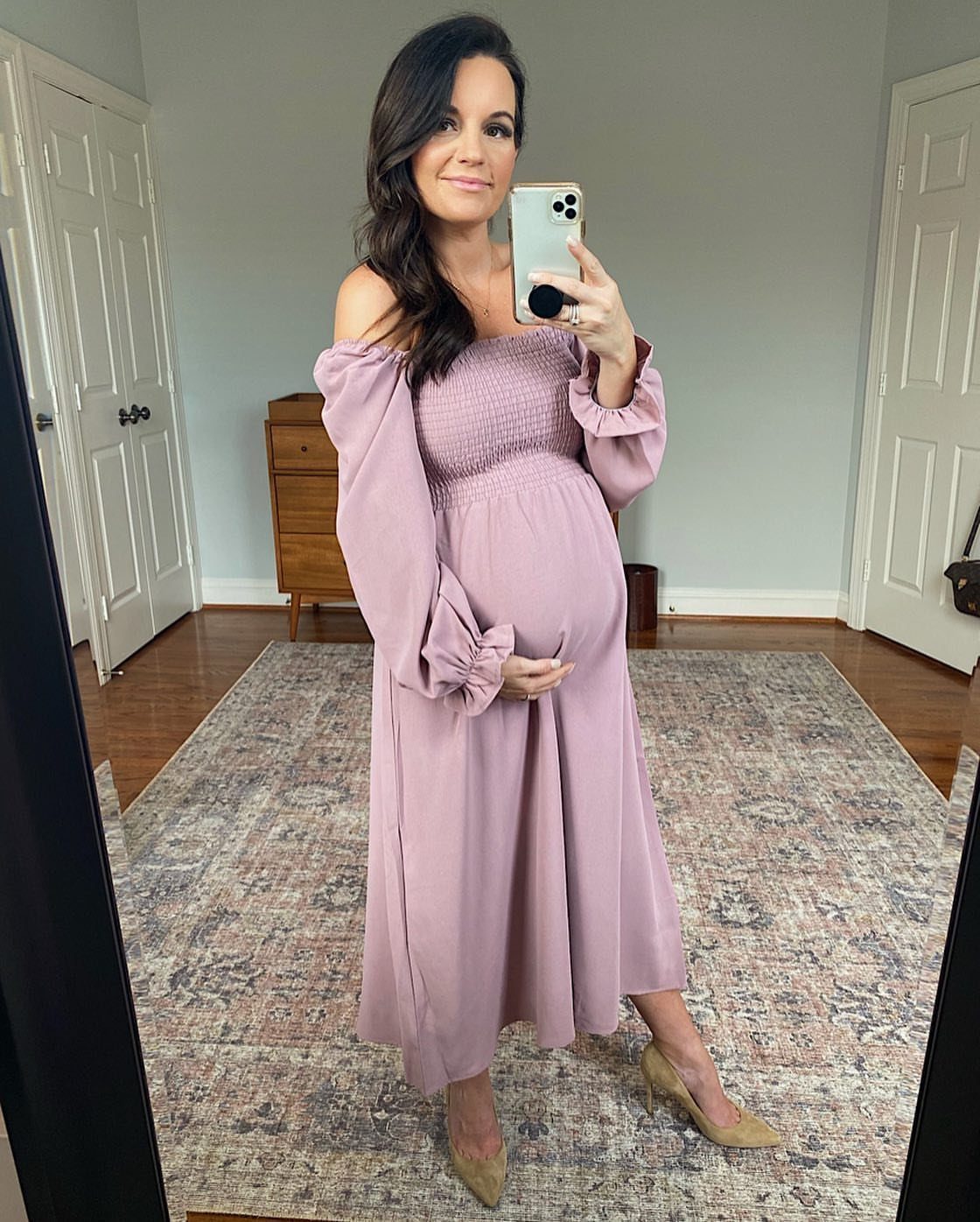 A pregnant woman in a mauve off-the-shoulder midi dress posing for a mirror selfie.