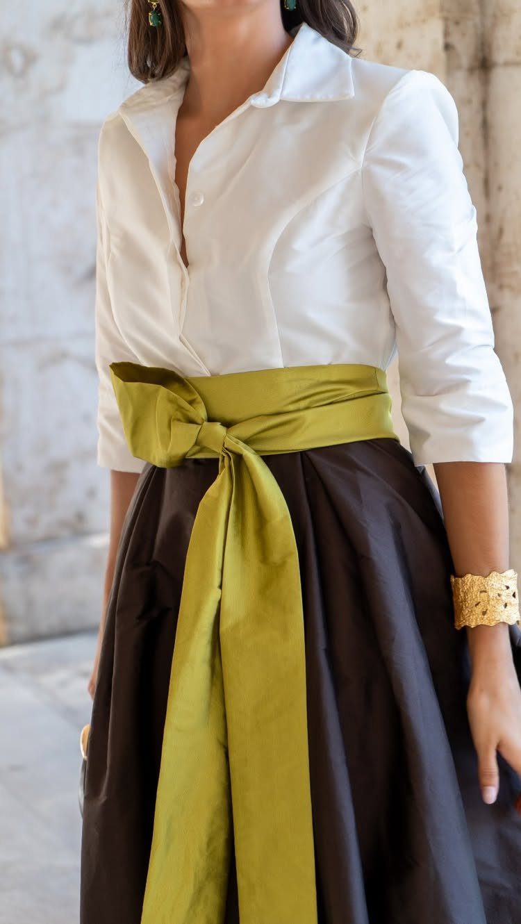 A person wearing a white shirt, black skirt, and a large olive green satin waist sash.