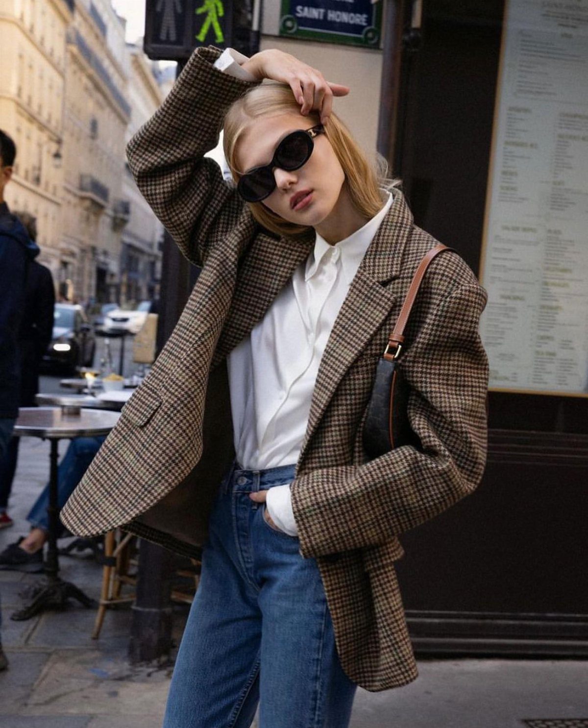 Woman wearing an oversized brown plaid blazer, white shirt, and blue jeans on a city street.