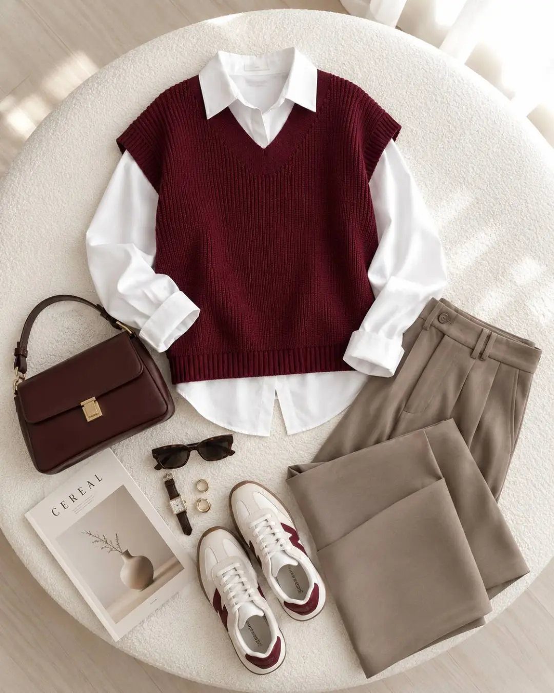 A maroon sweater vest over a white button-down shirt with beige trousers and accessories.