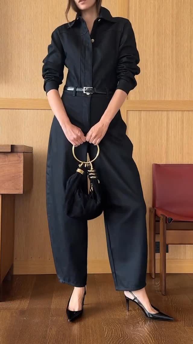 A person wearing a black tailored jumpsuit with a belt and black heels.