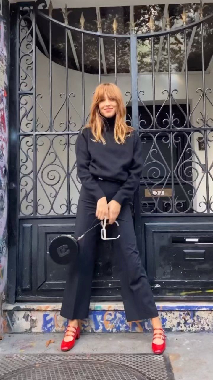 Woman in black turtleneck and cropped trousers wearing bright red Mary Jane shoes.