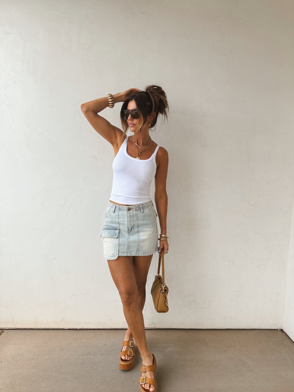Woman wearing a white tank top and a light blue denim utility skirt with cargo pockets.
