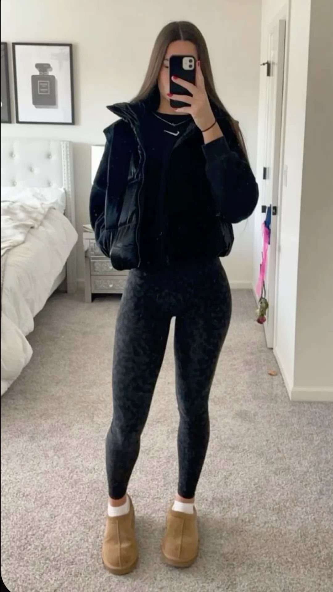 Woman in black puffer jacket and patterned leggings posing for a mirror selfie.