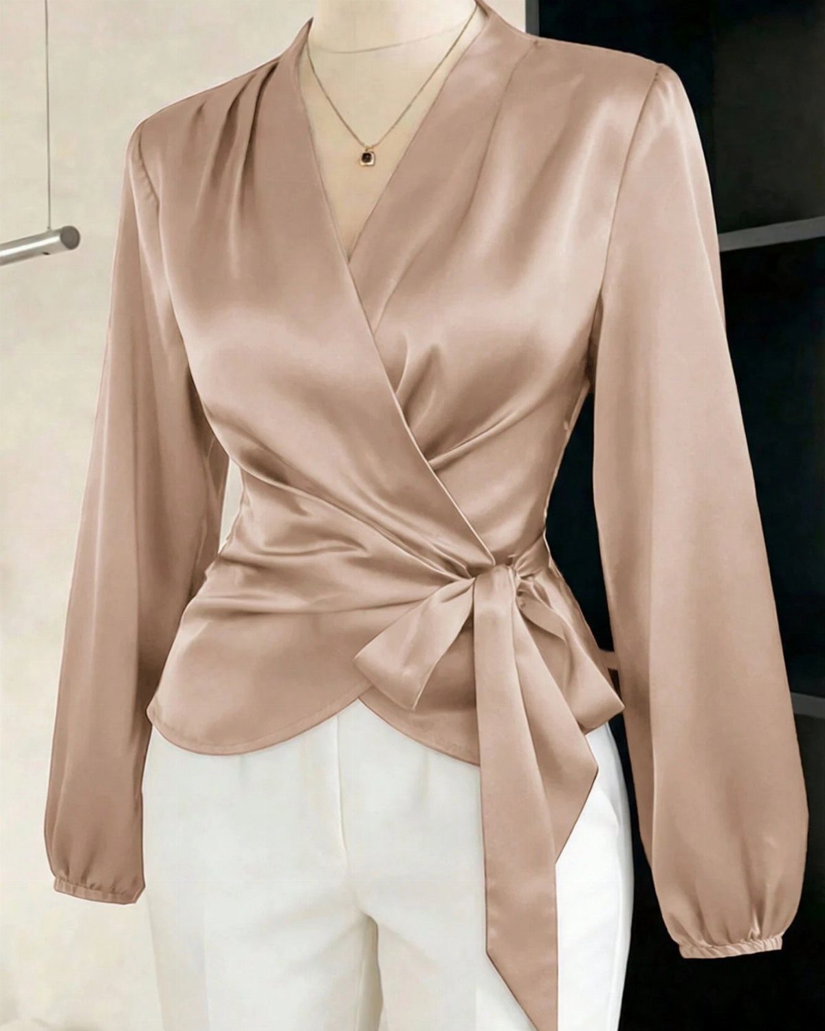 A person wearing a beige silk wrap blouse with long sleeves and white trousers.