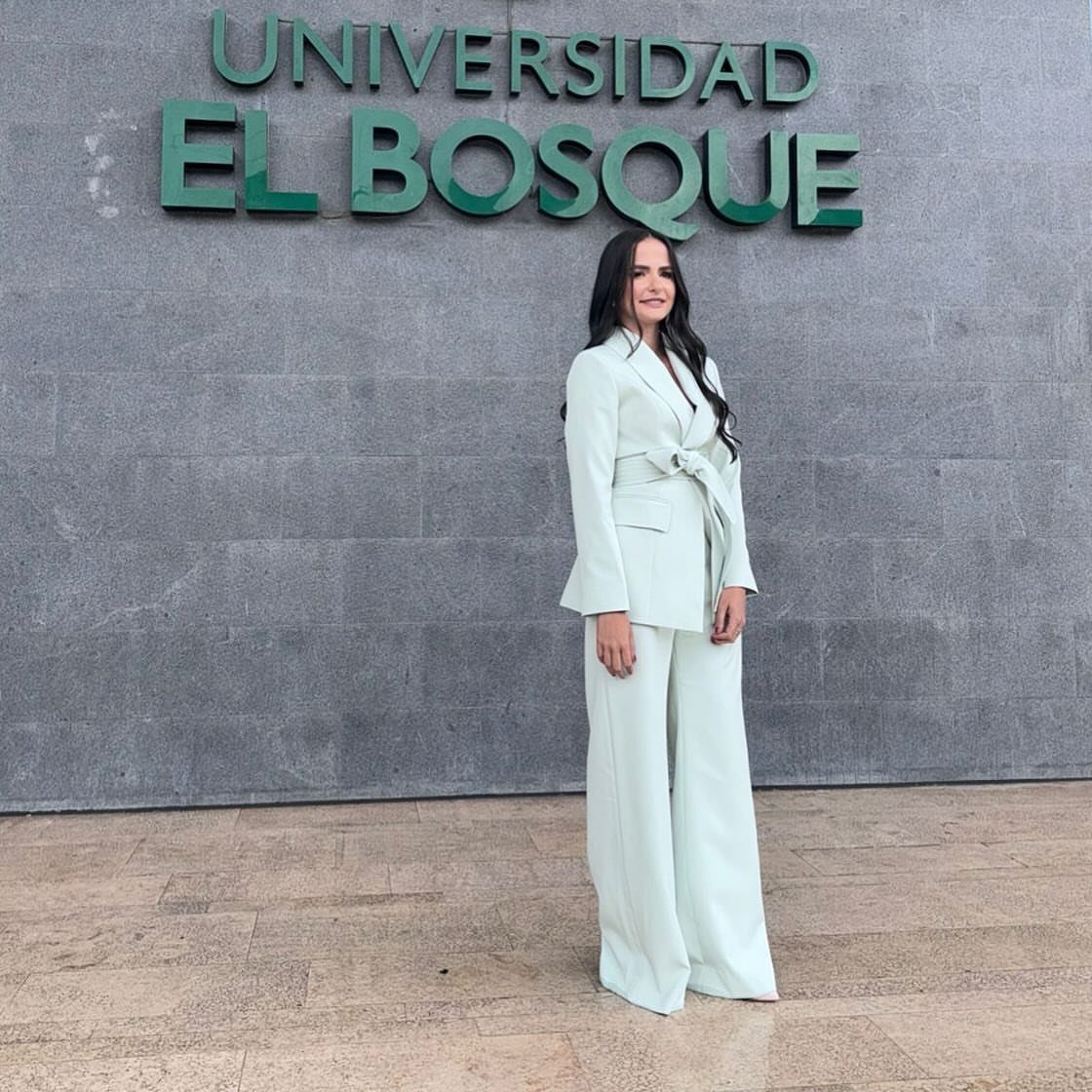 Woman in a light mint green tailored pantsuit standing before a grey stone wall.