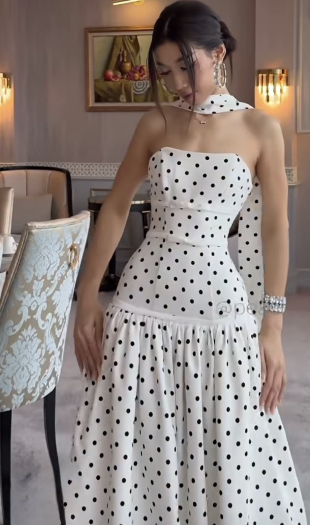A woman posing in a white strapless dress with black polka dots in a room.