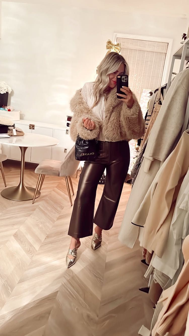 Woman posing in a tan faux fur jacket, brown leather pants, and silver heels.