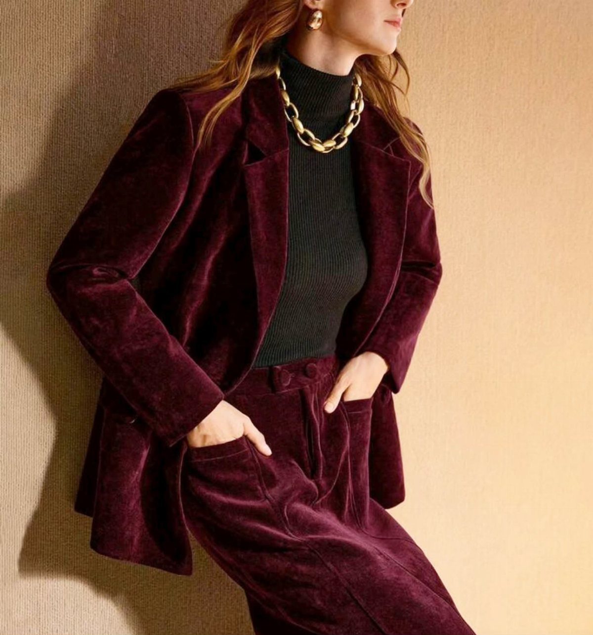 Woman wearing a burgundy velvet suit, black turtleneck, and a chunky gold chain necklace.