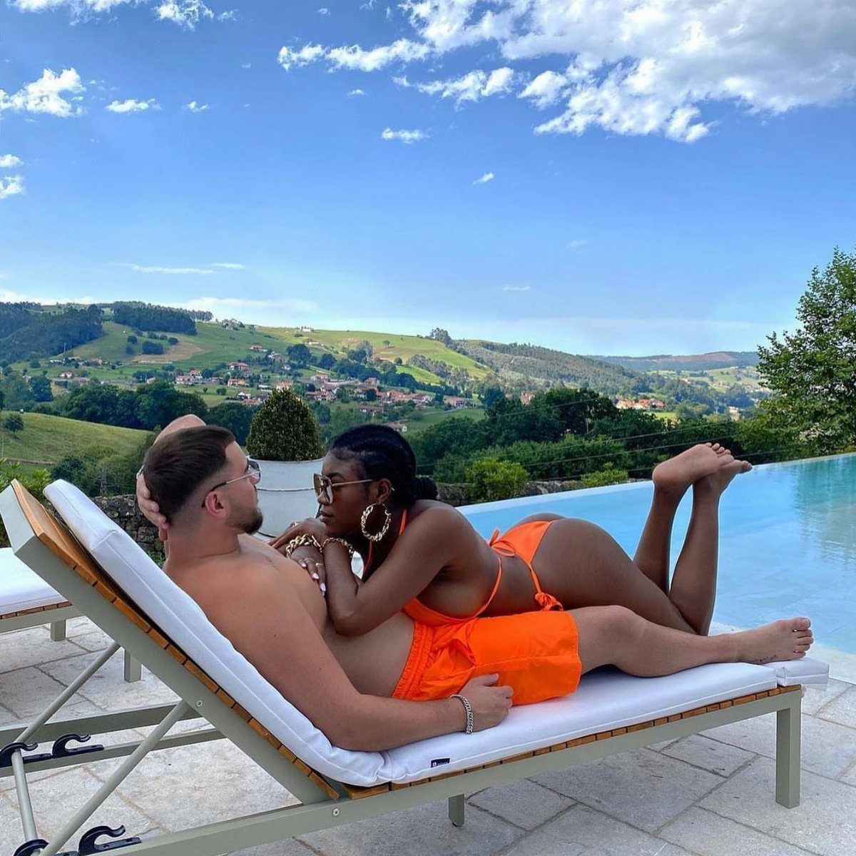 A man and woman in orange swimwear relaxing on a lounge chair by a pool.