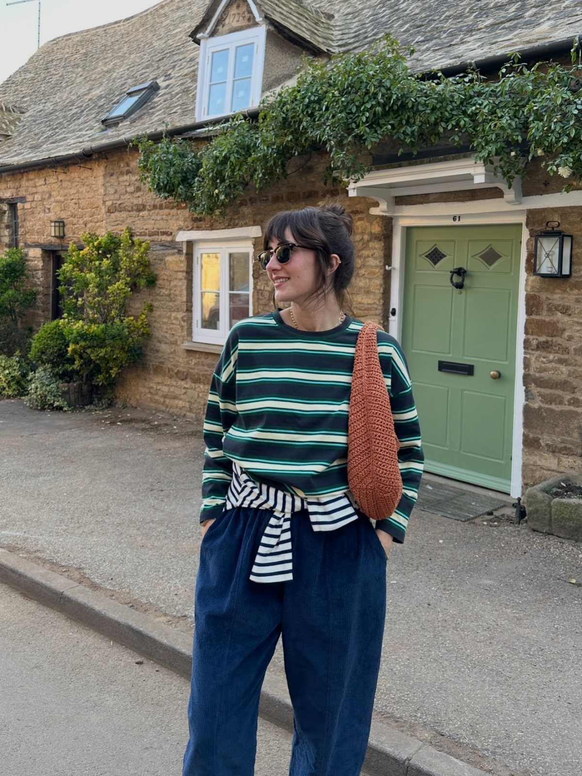 Woman in a striped top and navy trousers standing by a stone cottage.