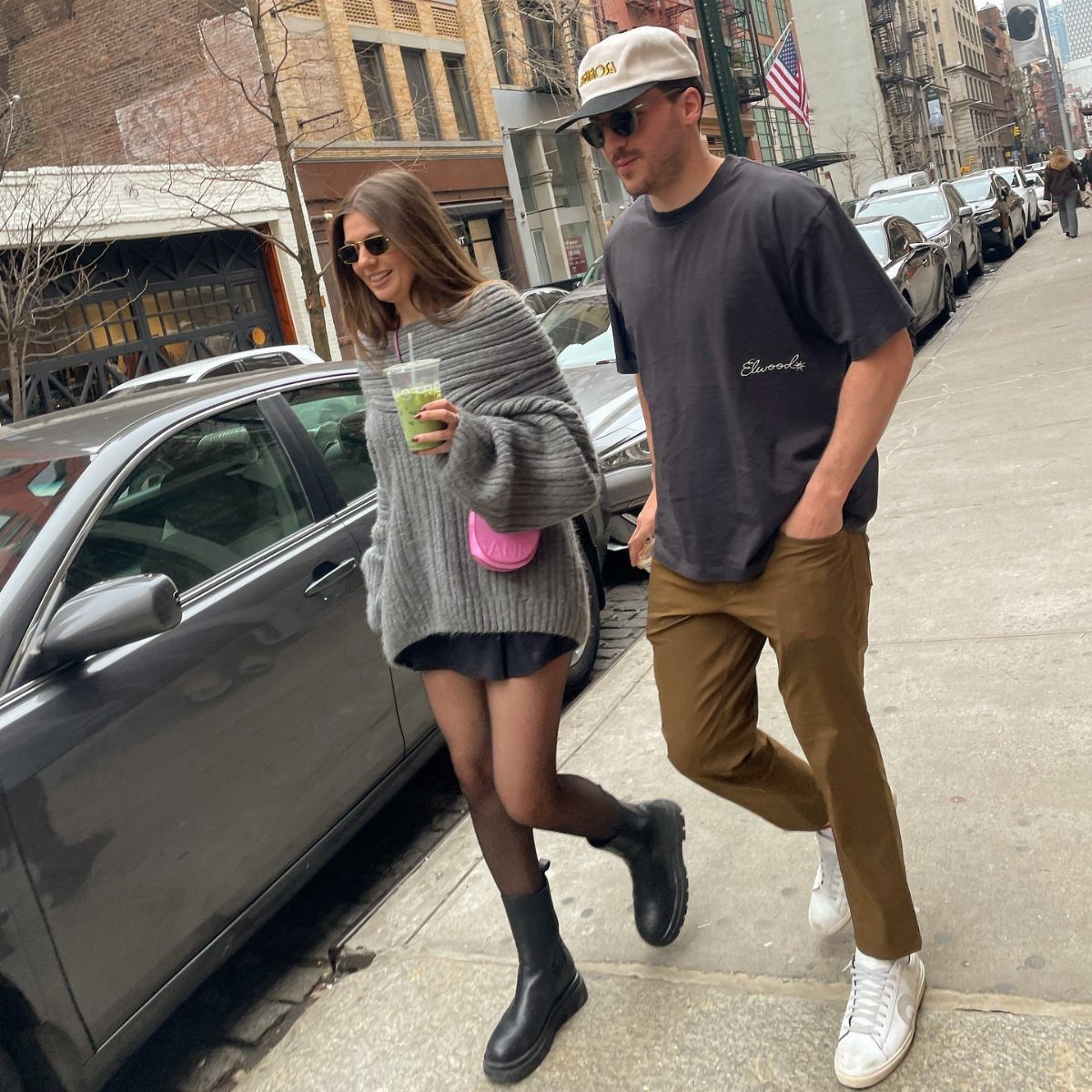 A woman walking on a city street wearing a grey oversized sweater and black Chelsea boots.