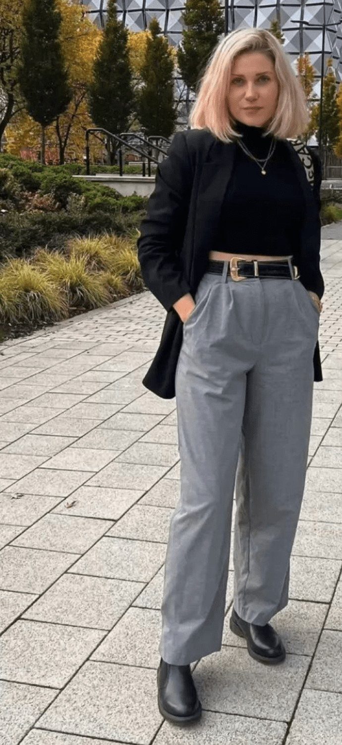 Woman wearing a black blazer, grey tailored trousers, and black Chelsea boots standing outdoors.