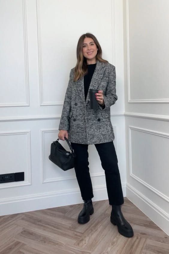 A woman posing in a monochrome outfit featuring a grey blazer, black trousers, and black Chelsea boots.