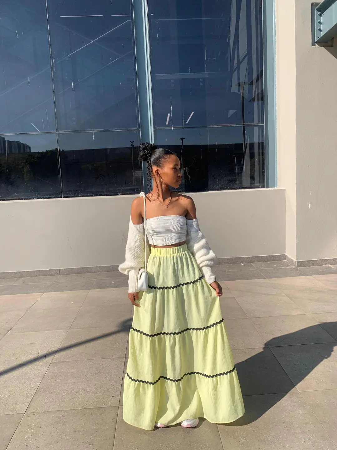 Woman posing in a white bandeau top and a long yellow tiered skirt outdoors.