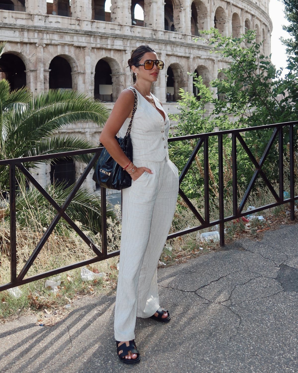 Woman in white sleeveless button-down top and wide-leg trousers standing near the Colosseum.