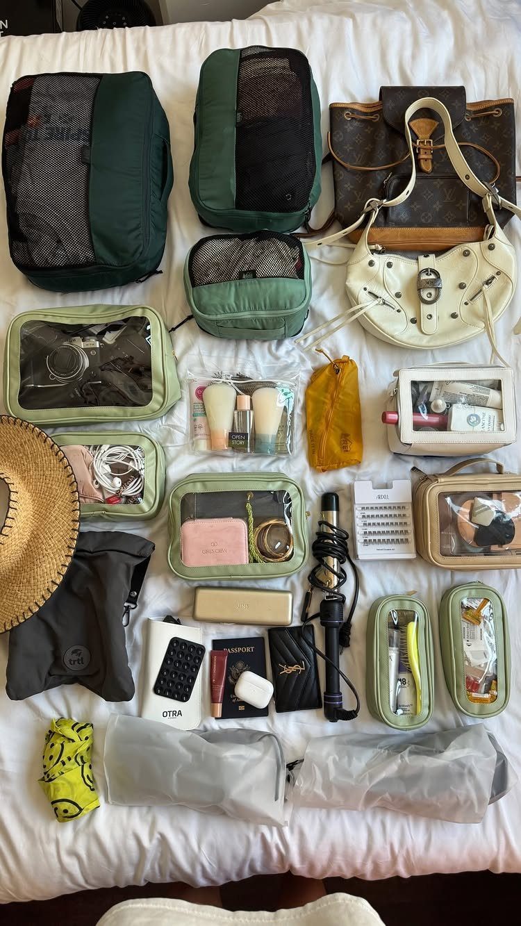 Green packing cubes and travel accessories laid out on a white bed surface.