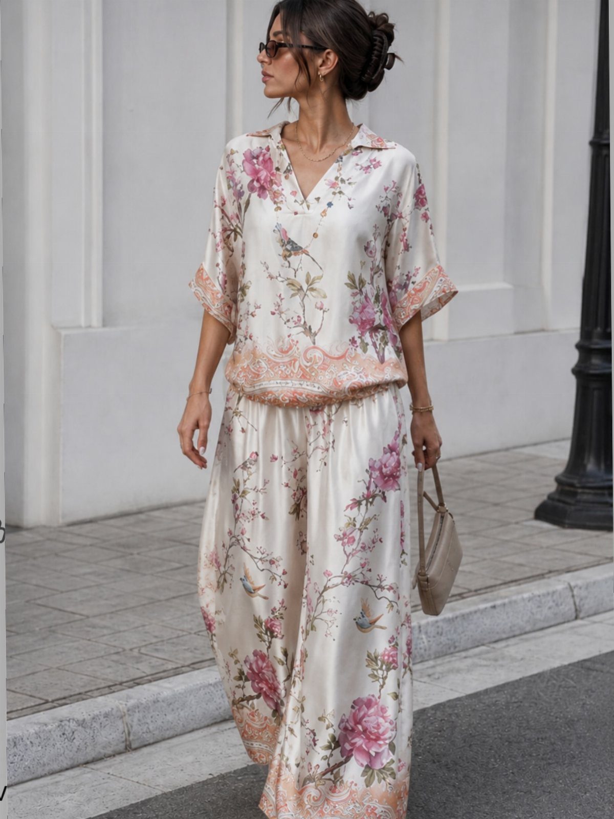 Woman wearing a cream floral silk short-sleeved top and matching wide-leg trousers standing on a sidewalk.