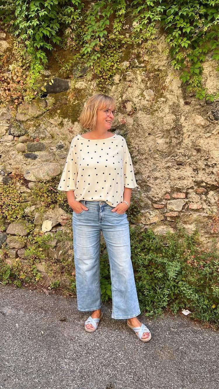 Woman wearing a polka dot blouse and light blue wide-leg denim pants standing outdoors.